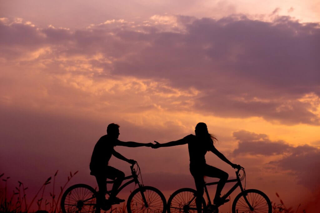 man and woman biking while holding hands